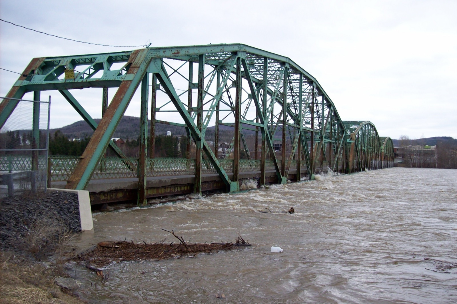 A green steel truss bridge with muddy floodwater rushing just beneath its deck. Credit: M. Huard, USGS (public domain)